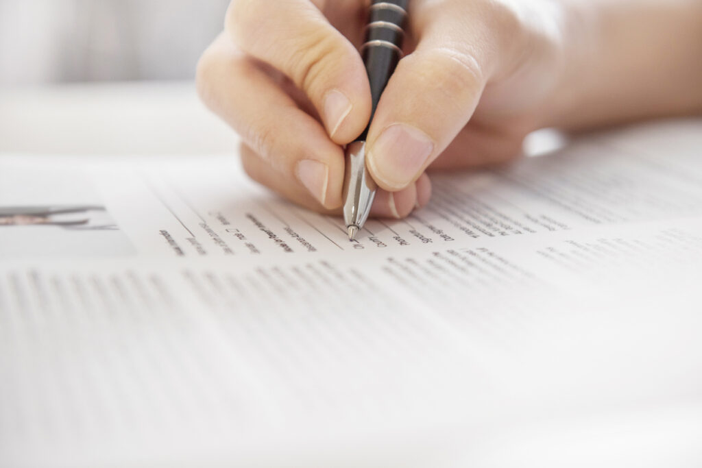 main tenant un stylo écrivant des mots pour se décrire sur un CV